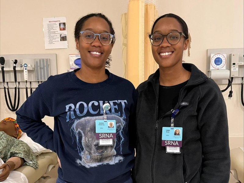 Identical twins Raonna Armstrong, BSN, RN, CCRN, and Tianna Brown, BSN, RN, CCRN together smiling in a classroom.