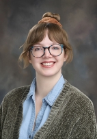 Enrollment Specialist Haley Fahrner with eye glasses, smiling wearing a blue shirt and a green sweater.