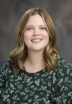 A portrait of Abrielle Powers smiling with a green floral top.