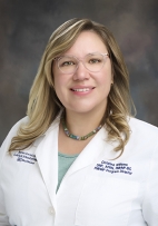 Christina Lucido Williams smiling, wearing glasses with a whit Doctors coat.
