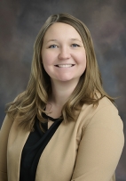 Sydnee Thompson smiling wearing a tan dress jacket with a black blouse.