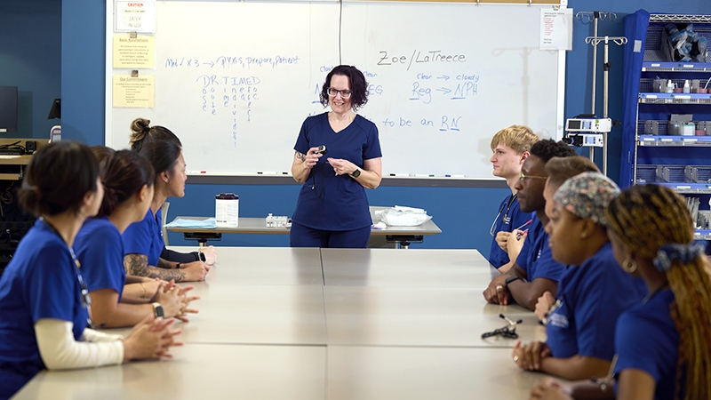 A Goldfarb nurse educator standing in front of a classroom setting with 10 students at a desk.
