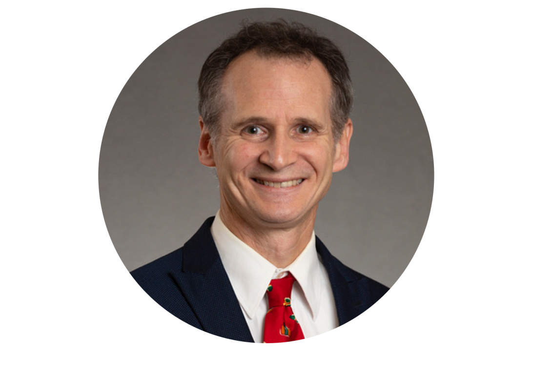 A portrait of Dominic-Reeds smiling with a black dress coat and red tie.