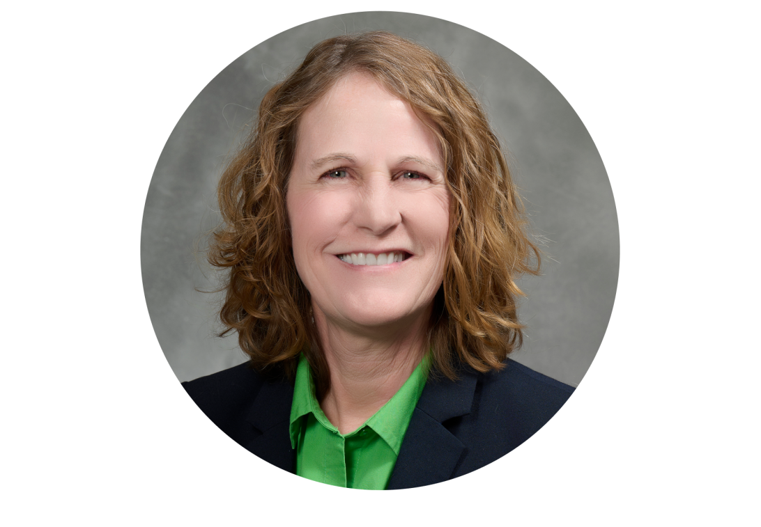 A portrait of Marilyn Schallom smiling with a black dress coat and green blouse.