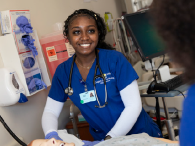 A nursing student stands by a practice dummy