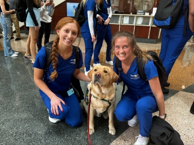 Two health care providers next to the Dean of Snuggles, a Labrador Retriever