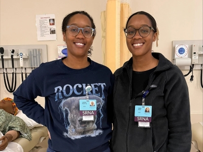 Identical twins Raonna Armstrong, BSN, RN, CCRN, and Tianna Brown, BSN, RN, CCRN together smiling in a classroom.