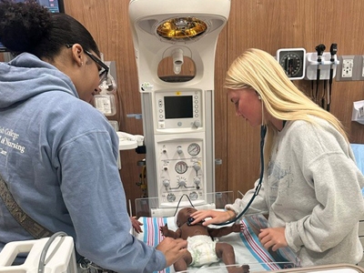 Two Goldfarb students working in the simulation lab on a baby doll.